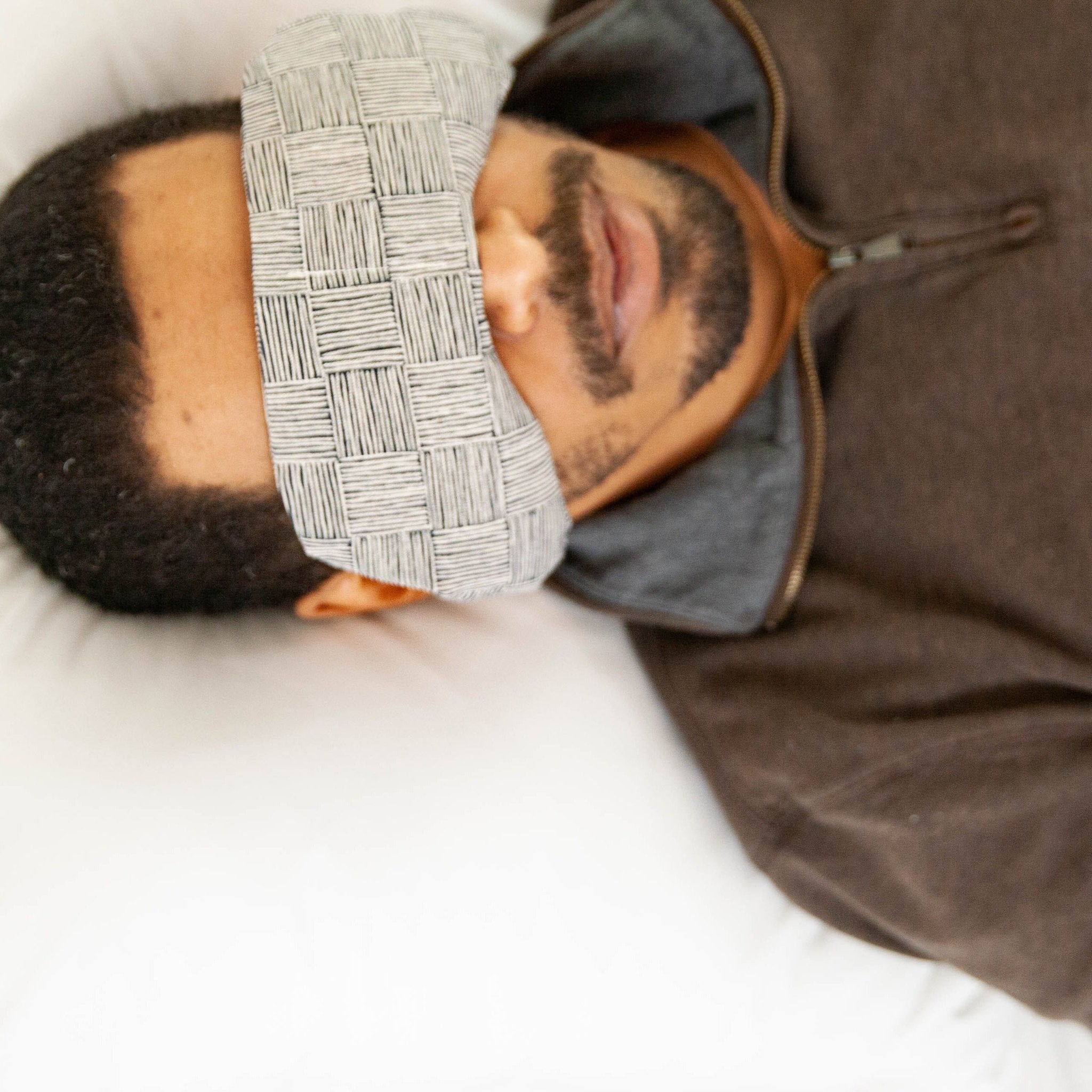 Man wearing a migraine relief eye mask, resting on a pillow to ease tension and headaches.